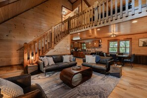 A spacious living area with a staircase, leather sofas, a coffee table, and a kitchen in the background. - Mountain Memories:HotTub, GameRoom-KingSuites (Blue Ridge)