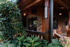 A log cabin with a stone fireplace, wooden porch, and a number sign indicating the address. - Mountain Memories:HotTub, GameRoom-KingSuites (Blue Ridge)