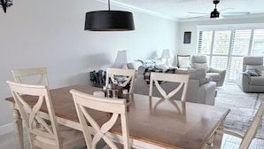 Uma sala de jantar com uma mesa e cadeiras de madeira, um lustre pendente e um ventilador de teto.