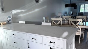 Uma cozinha moderna com armários brancos, uma ilha grande e um espaço de refeições com mesa e cadeiras.