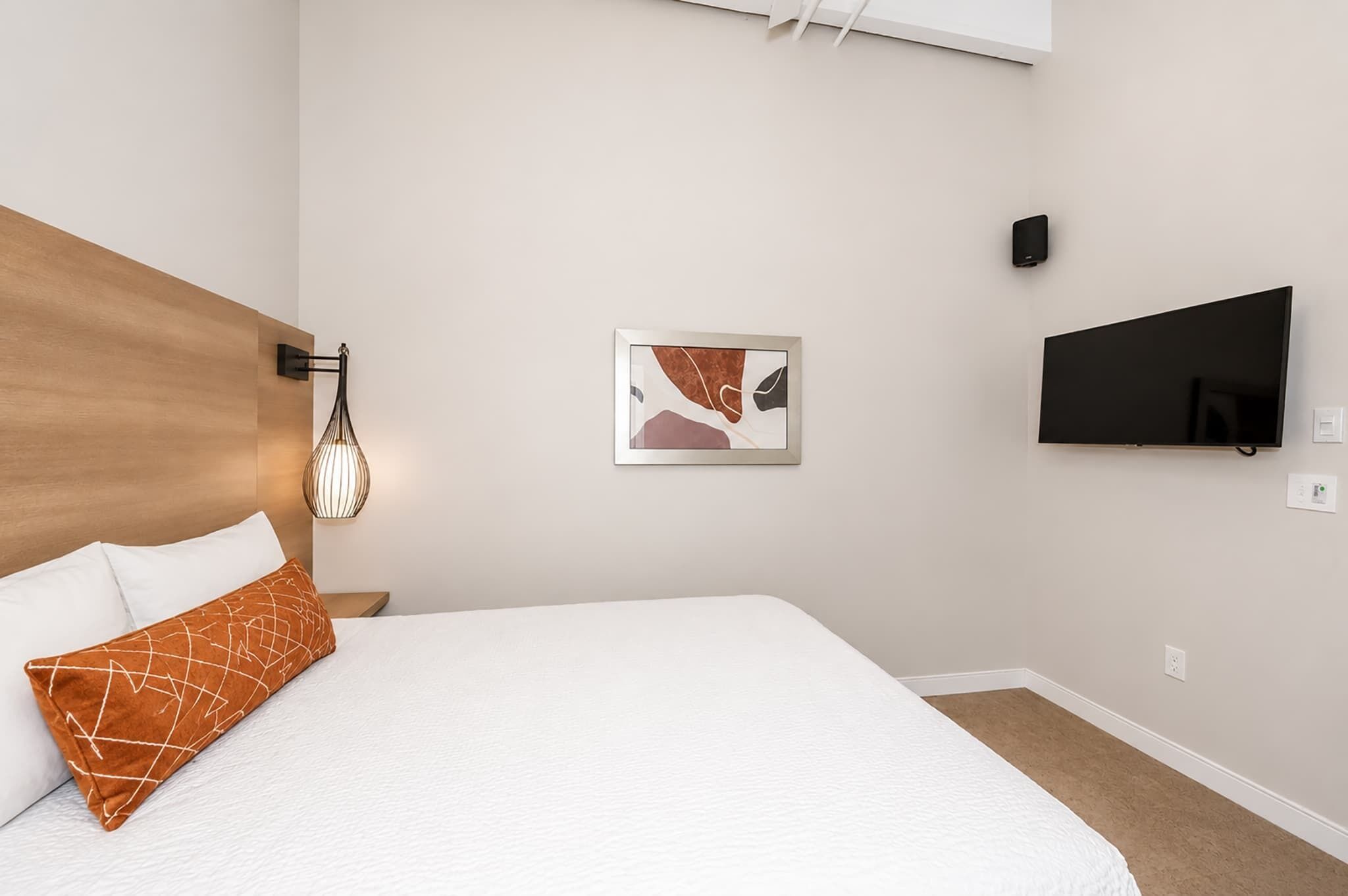 Habitación de hotel con una cama, televisión montada en la pared, un cuadro y una lámpara.