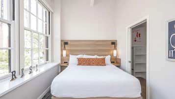 A neatly made bed with a wooden headboard, bedside lamps, and a window with a view of greenery.