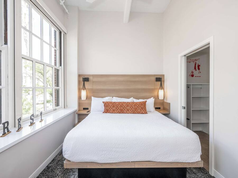 A neatly made bed with a wooden headboard, bedside lamps, and a window with a view of greenery.