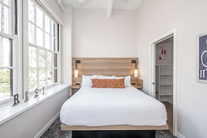 A neatly made bed with a wooden headboard, bedside lamps, and a window with a view of greenery. - Queen City Escape | 2BR | Walk to Aronoff & Reds (Cincinnati)