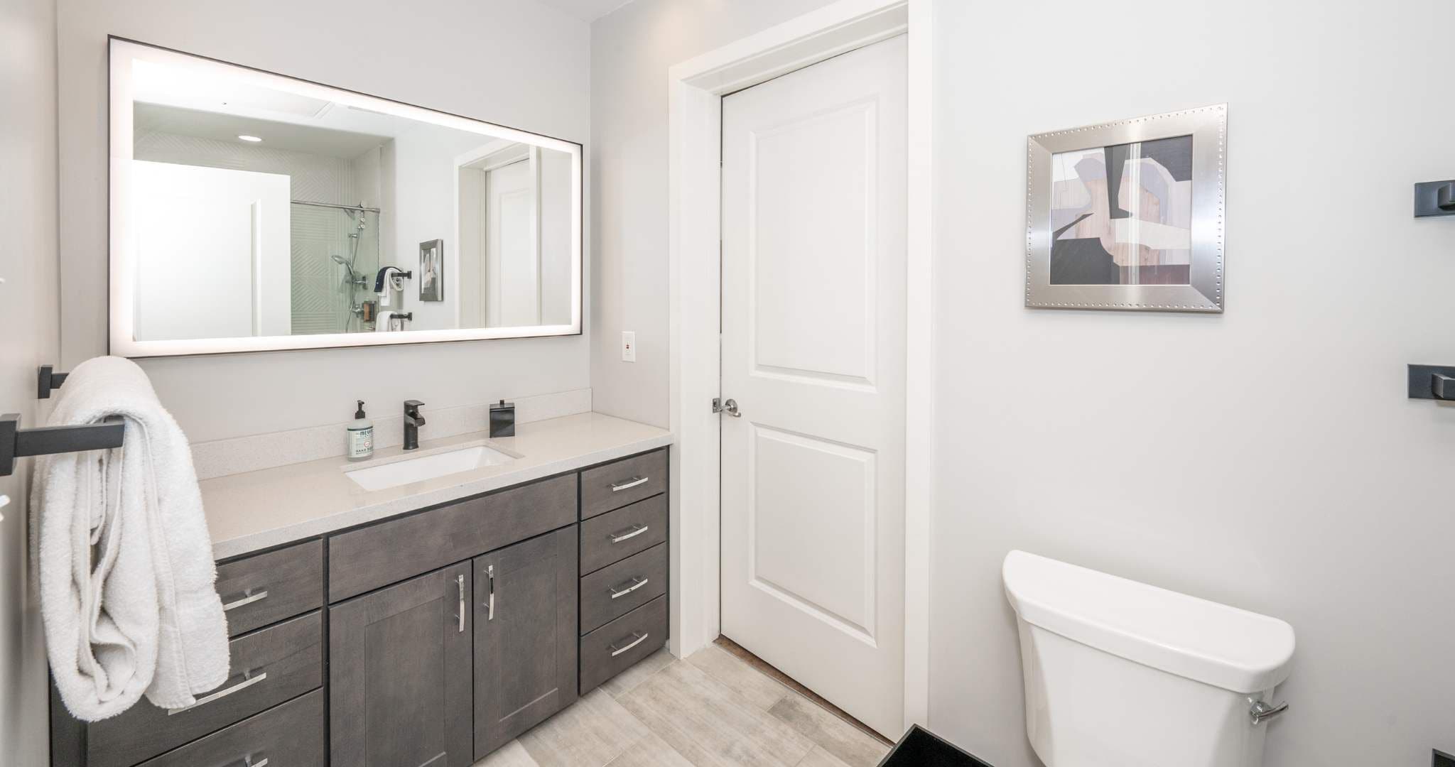 A modern bathroom with a large mirror, a sink, and a toilet.