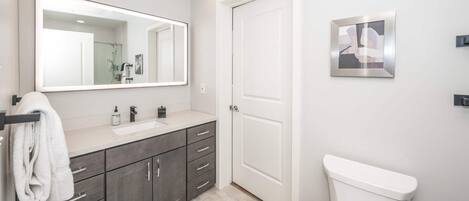 A modern bathroom with a large mirror, a sink, and a toilet.