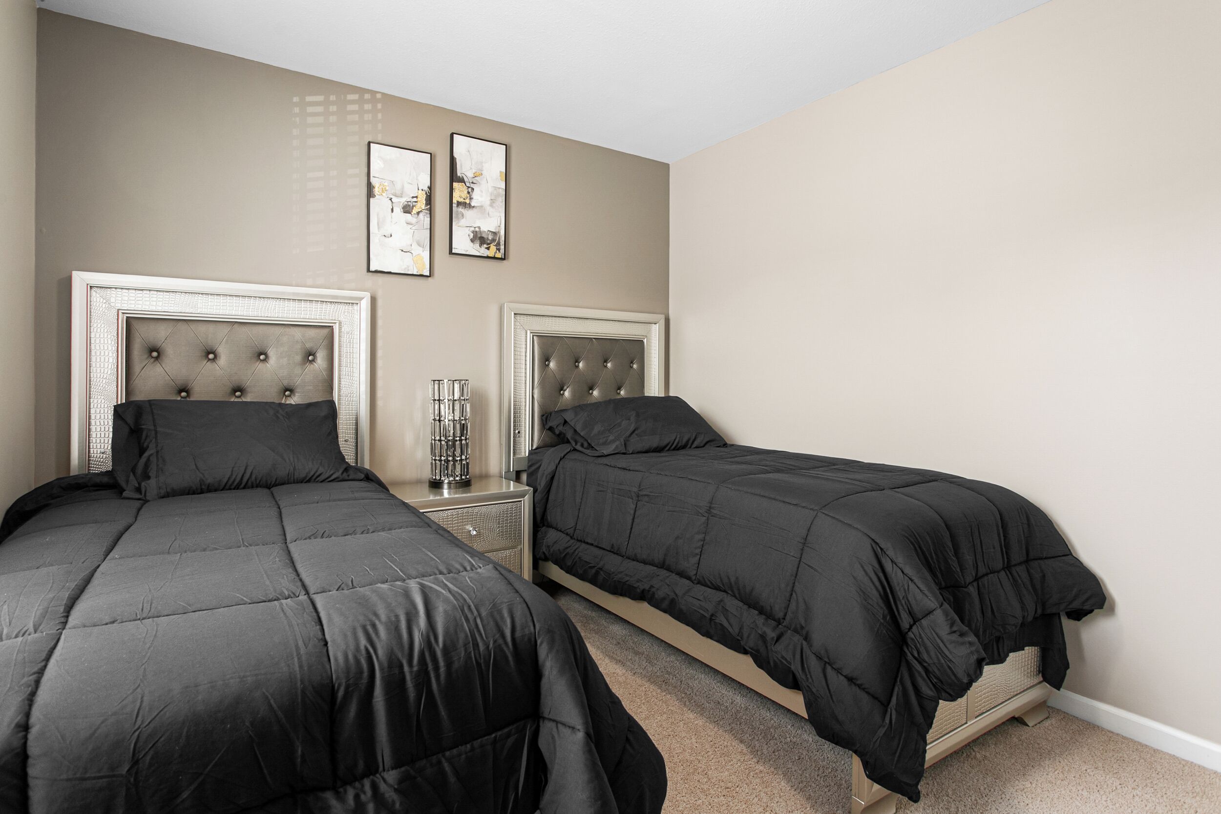 A bedroom with two beds, each with a tufted headboard, a bedside table, and a lamp.
