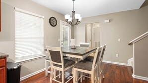 A dining area with a rectangular table, four chairs, a chandelier, and a clock on the wall. - 324 Beautiful Residence in Mebane NC. (Mebane)