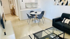 Una sala de estar moderna con un sofá negro, una mesa de centro de vidrio y un comedor con una mesa redonda y sillas.