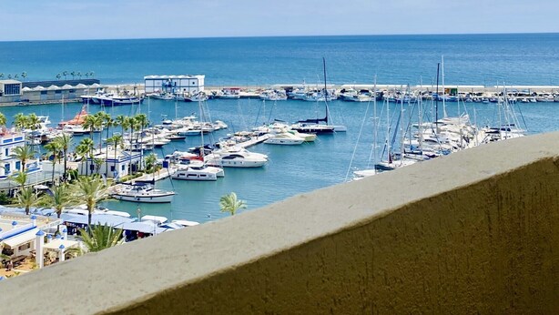Un puerto deportivo con barcos amarrados, un muelle que se adentra en el agua y un cielo despejado.