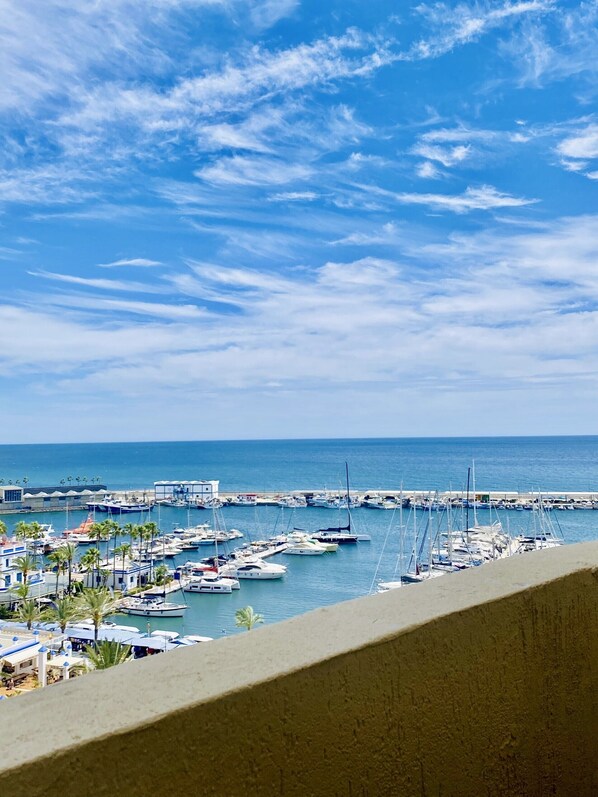 A marina with boats docked, a pier extending into the water, and a clear sky.