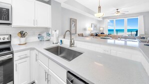 A modern kitchen with white cabinetry, stainless steel appliances, and a large island with a sink. - Calypso 3-1006 (Panama City Beach)