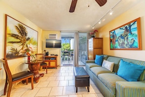 A living room with a sofa, chairs, a coffee table, and artwork on the walls. - Ocean-view Condo – Private Lanai - In Kona Town (Kailua-Kona)