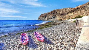 A rocky beach with kayaks, a cliff, and a clear blue sky.