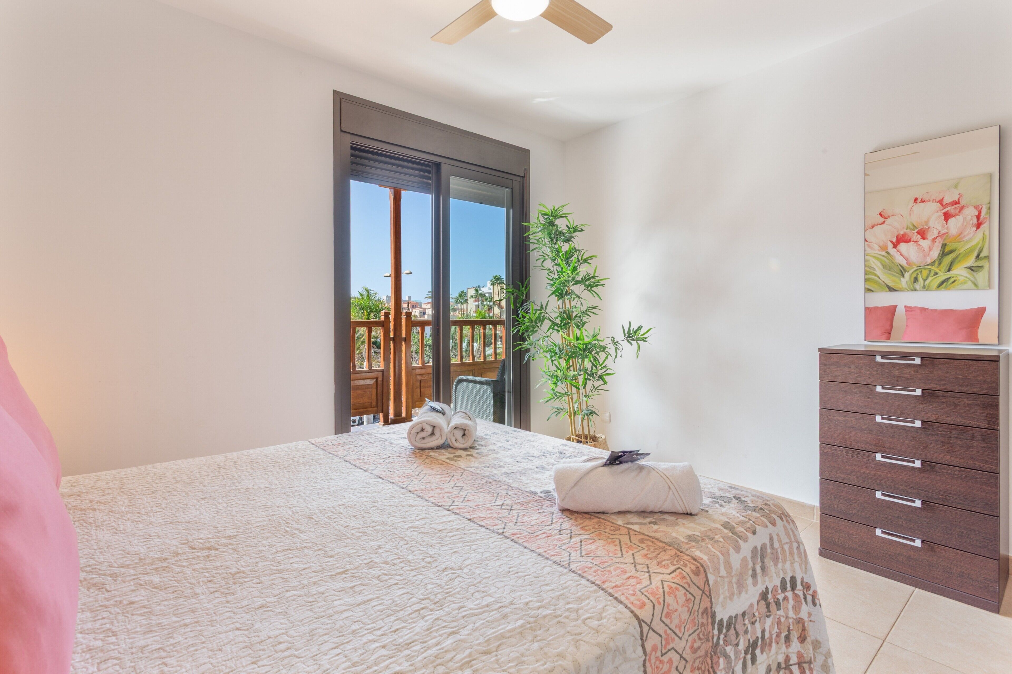 Un dormitorio con cama, cómoda, planta en maceta y balcón con vistas.