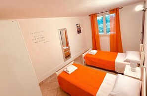 Hotellihuone, jossa on kaksi sänkyä, oranssit verhot ikkunassa, peili ja seinä, jossa on kannustava sitaatti.