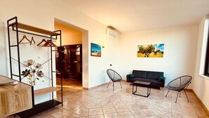 A modern living room with a sofa, two chairs, a coffee table, and a wooden cabinet. There is a metal rack with clothes and a vase with flowers. - Villa Gioia (Puglia)