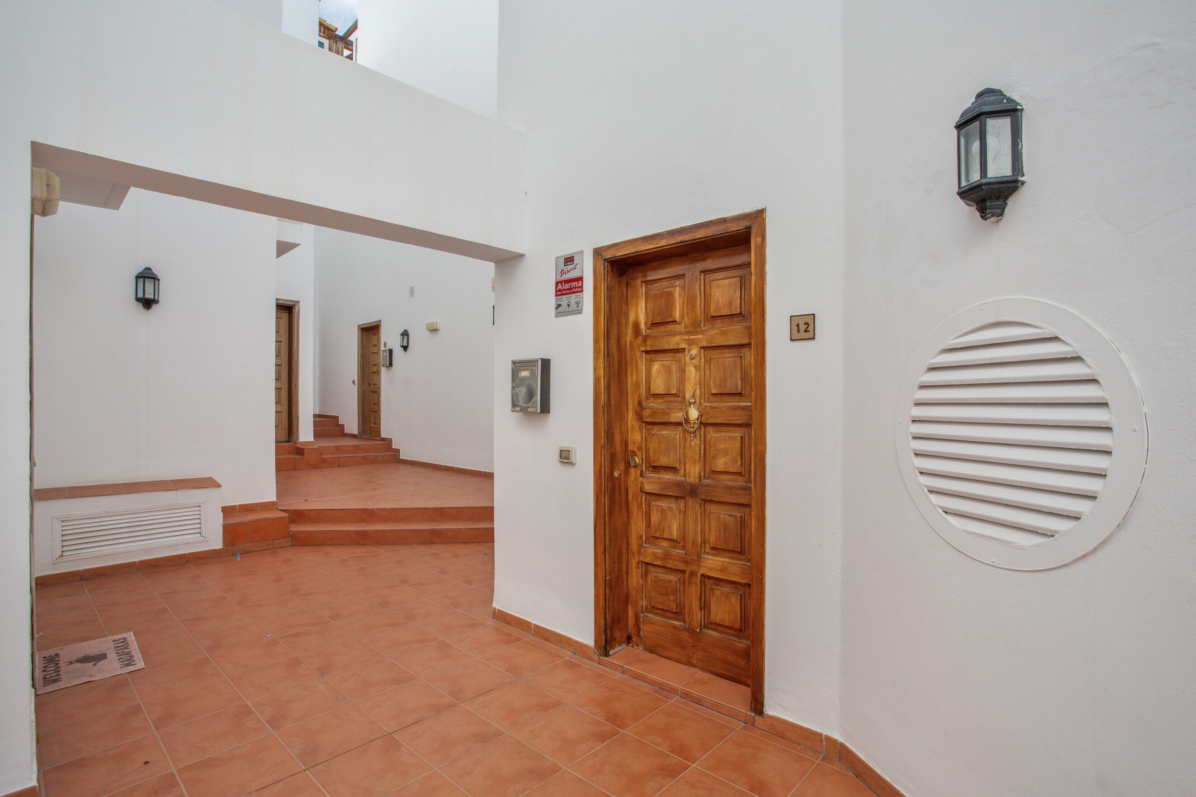 Un corridoio con una porta in legno, una luce a parete e una griglia di ventilazione.