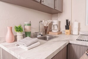 Eine Küche mit Marmorarbeitsplatte, Spüle aus Edelstahl und Holzausbau. Es sind Küchenutensilien, eine Kaffeemaschine und eine Pflanze in einer Vase vorhanden.