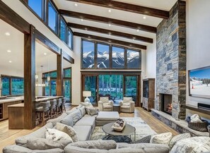 A spacious living area with a large couch, a fireplace, and a view of mountains through large windows. - ✨ Soltierra • 🏔️ Breck Peak 8 • 🎿 Ski-In • 💦 10-Person Spa • 🛏️ 13 Beds (Breckenridge)