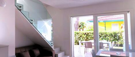 A modern interior with a staircase, a brown sofa, a dining table, and a sliding glass door leading to an outdoor patio.