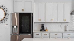 Una cucina moderna con mobili bianchi, elettrodomestici in acciaio inossidabile e una macchina da caffè.