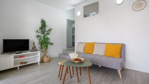 Ein modernes Wohnzimmer mit Flachbildfernseher, einer gelben Kissensofa, einem kleinen Tisch mit Schüssel und einer Topfpflanze.