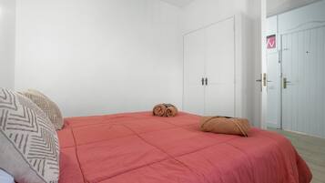 A bedroom with a red bedspread, two pillows, a rolled towel, and a white door with a sign.