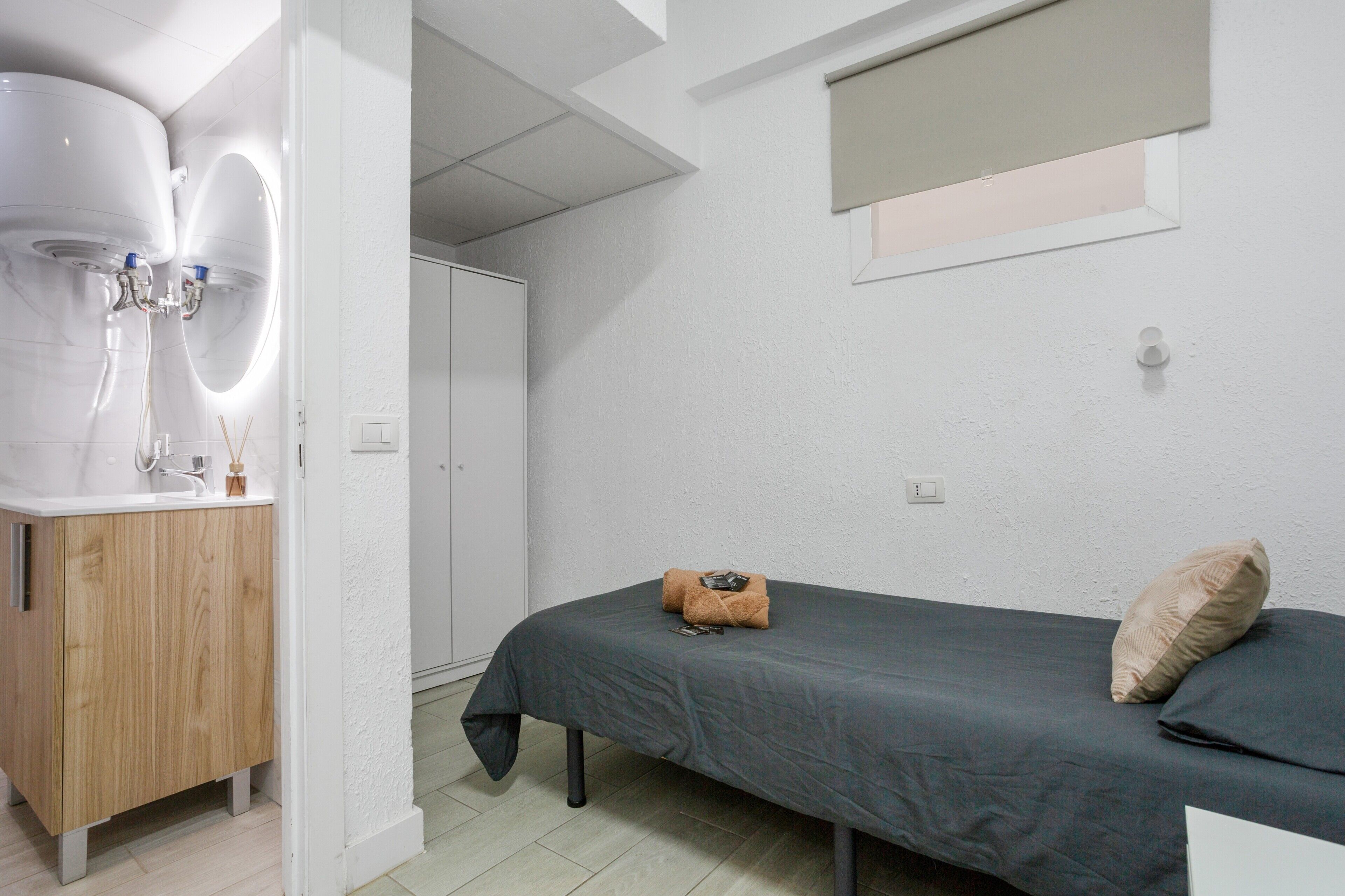 Ein Schlafzimmer mit einem Bett, einem Holzschrank, einem kleinen Fenster und einer weißen Wand.
