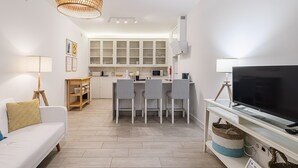 Un soggiorno moderno con divano, televisione e zona pranzo con sedie, e una cucina sullo sfondo.
