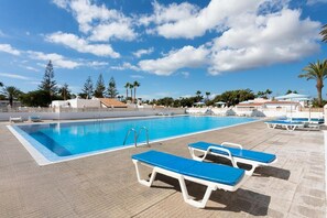 Une piscine à l’eau bleue, entourée de chaises longues et de palmiers.