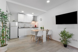 Une cuisine moderne avec des meubles blancs, une table à manger en bois et deux plantes en pot.