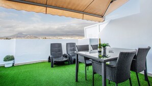 A rooftop terrace with a table and chairs, a potted plant, and a view of distant mountains.