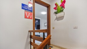 A wooden staircase with a handrail, a white wall with a sign, and a potted plant with flowers.