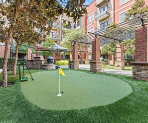 A miniature golf course with a green artificial turf, surrounded by brick buildings and trees. - GV001 |Spacious 1BD Apt| D/town Grapevine (Grapevine)