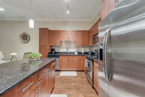 A modern kitchen with wooden cabinets, a stainless steel refrigerator, and a granite countertop. - GV001 |Spacious 1BD Apt| D/town Grapevine (Grapevine)