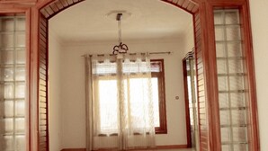 Una habitación amplia con techo alto, una lámpara colgante y un gran ventanal con cortinas de gasa.