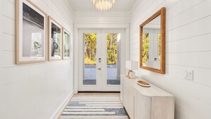 A hallway with white walls, a wooden floor, a striped rug, a wooden console table with a mirror, and framed artwork. - Pelayo Solage|Deeded Beach Access|Private Pool|Golf Cart & Bikes (Santa Rosa Beach)