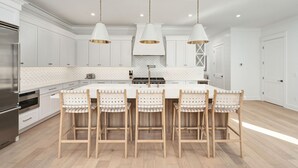A modern kitchen with white cabinetry, a central island with bar stools, pendant lighting, and a stainless steel refrigerator. - Pelayo Solage|Deeded Beach Access|Private Pool|Golf Cart & Bikes (Santa Rosa Beach)