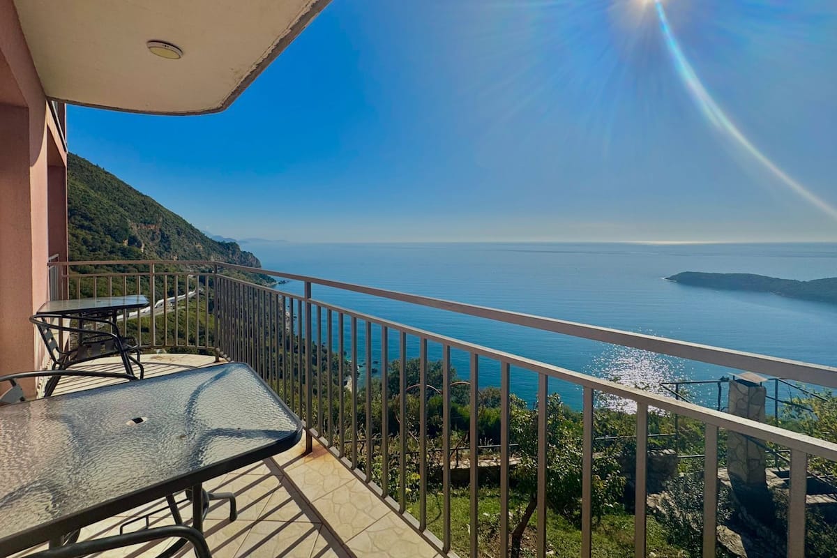 Un balcon avec une table et des chaises, offrant une vue sur la côte, avec un ciel dégagé et la mer.