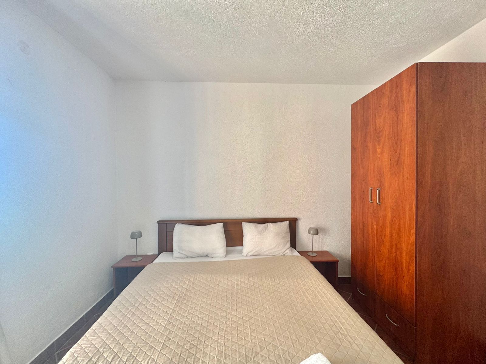 A bedroom with a bed, two bedside tables, and a wooden wardrobe.