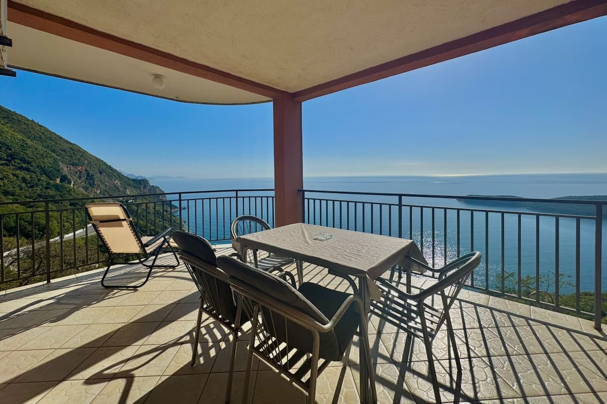 Un espace extérieur abrité, doté d’une table et de chaises, offrant une vue sur un paysage côtier.