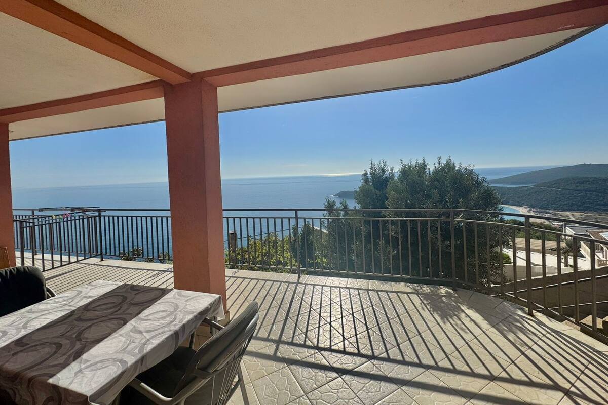 Un balcon avec une table et des chaises, offrant une vue sur la côte, la mer et les collines.