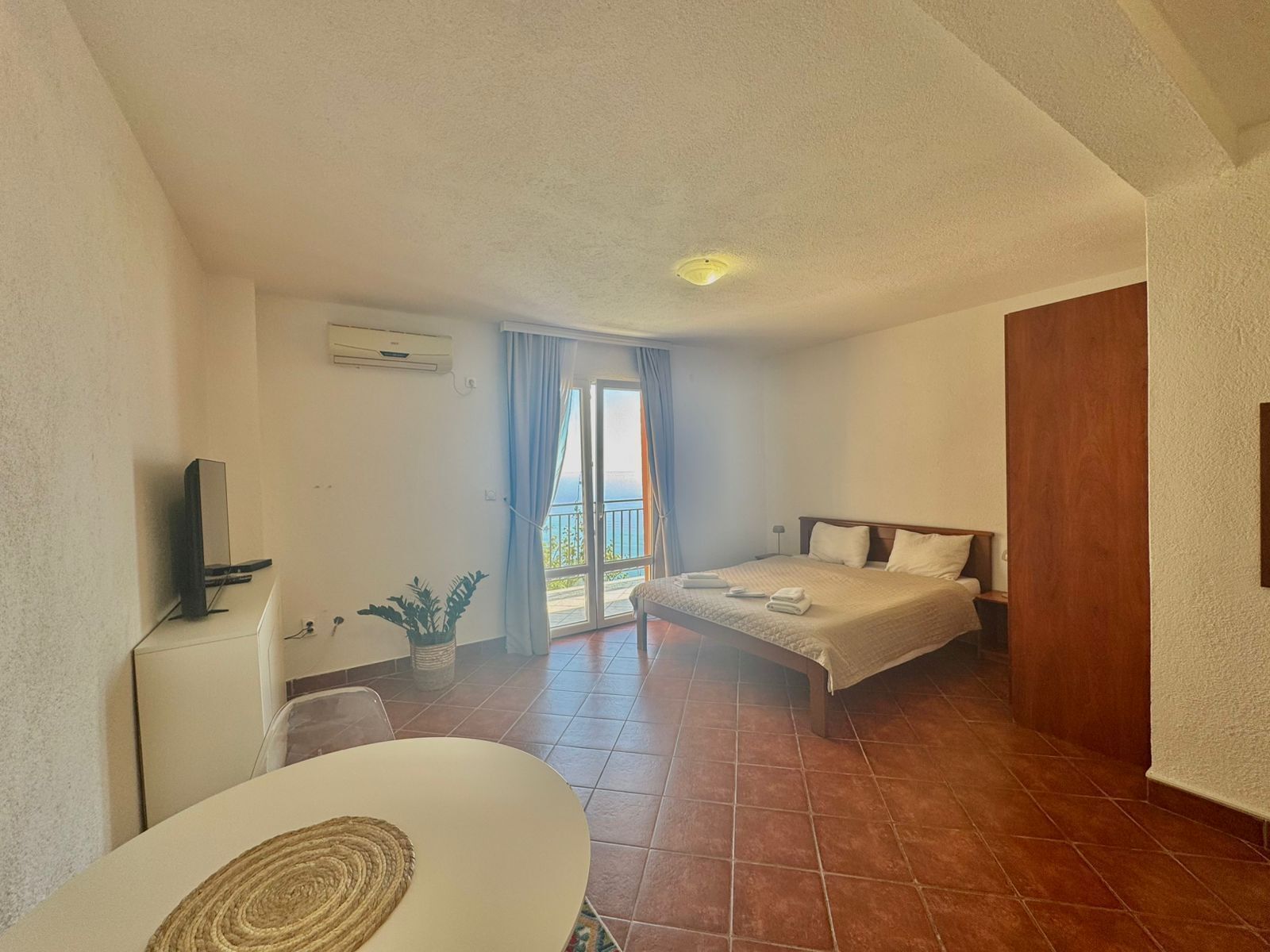 A hotel room with a bed, a desk, a TV, and a view of the outdoors.