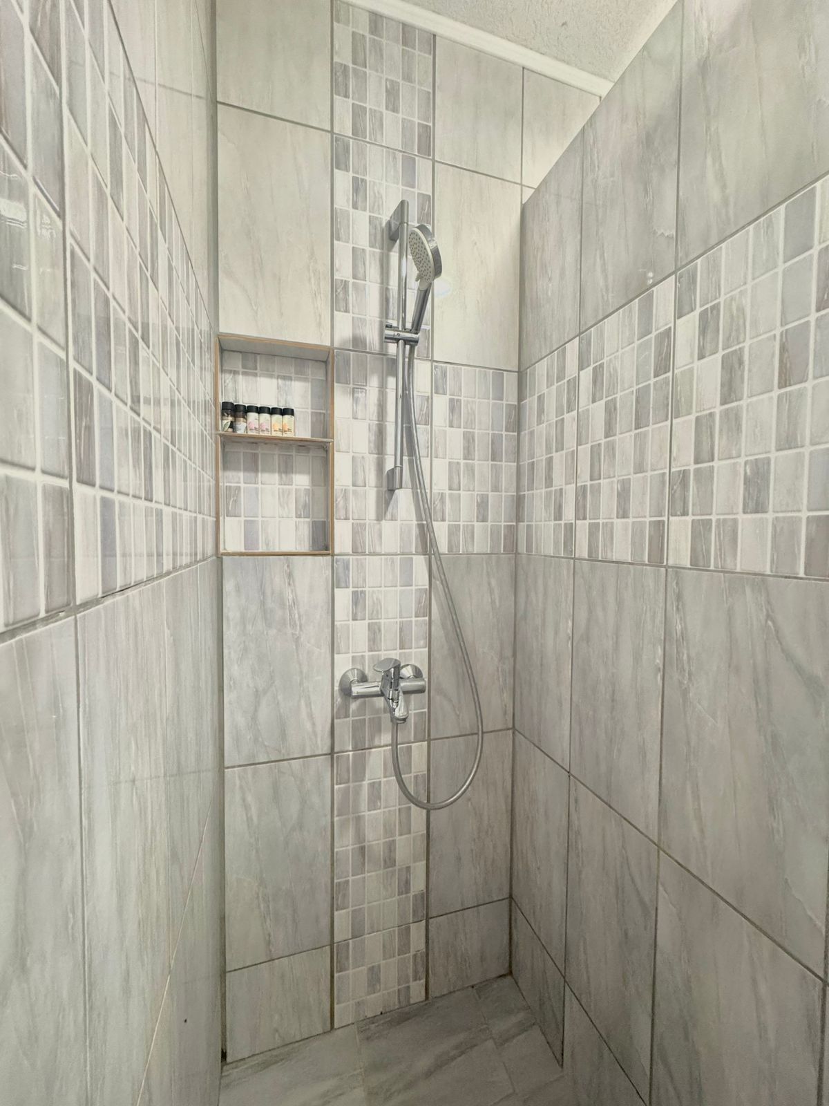 A shower area with a glass-enclosed shelf unit containing toiletries.