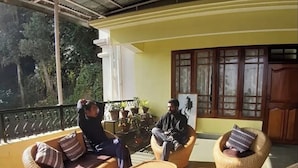 A covered outdoor seating area with wicker furniture and a view of the surrounding greenery. - Ronglyang homestay  (Gangtok)