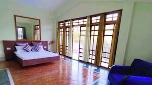 A bedroom with a bed, a large window with curtains, a blue sofa, and a wooden floor. - Ronglyang homestay  (Gangtok)
