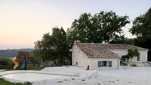 A rustic house with a tiled roof, a small garden, and a playground with a slide.