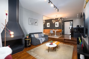 A modern living room with a sofa, coffee table, and a fireplace. There is a dining area with a table and chairs.
