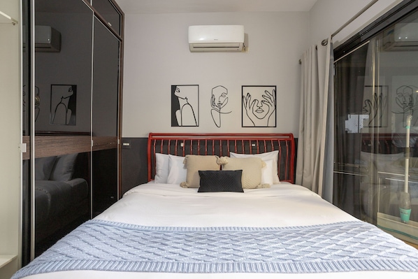 Un dormitorio con cama, cabecero rojo, aire acondicionado instalado en la pared y obras de arte.